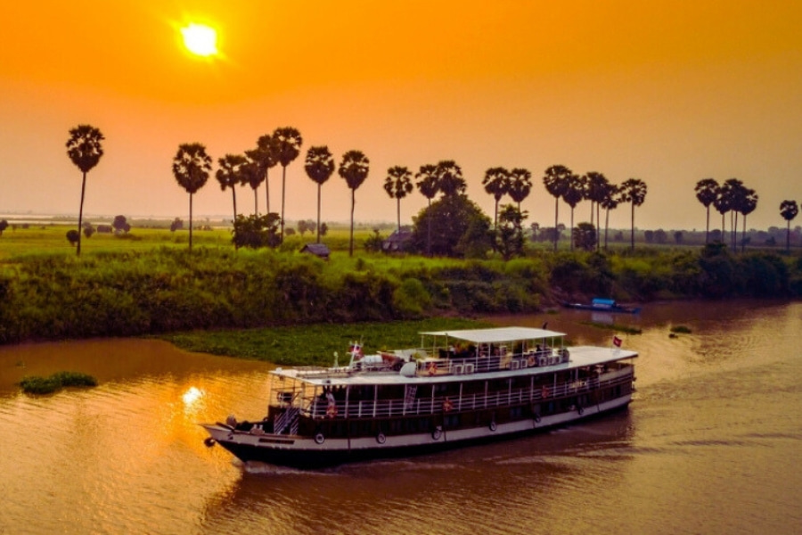 Cambodia Mekong River cruise sailing at sunset with palm trees along the riverbank